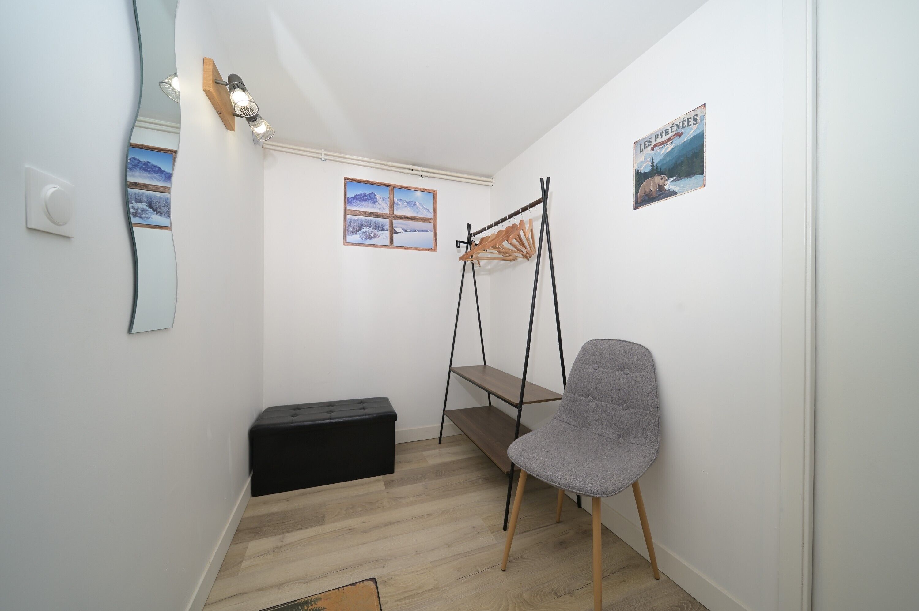A small room with a wooden bench, a grey chair, a black storage unit, and a wall-mounted rack.
