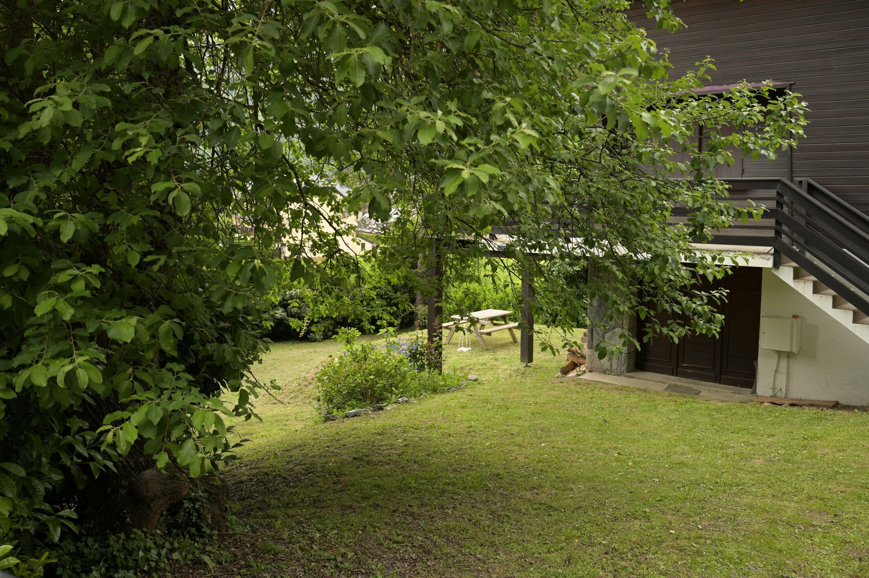 Il s'agit d'une propriété résidentielle dotée d'une cour verdoyante, d'une terrasse en bois et d'un escalier menant à un bâtiment de couleur sombre.