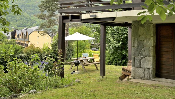 Ein überdachter Außenbereich mit Tisch und Stühlen, einem Grill und einem weißen Sonnenschirm.