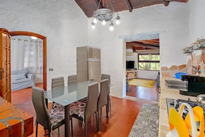 Uma área de refeições com mesa de vidro e cadeiras, geladeira e lustre.