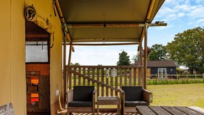 Une terrasse en bois avec deux chaises et une table, un espace couvert avec un mur jaune, et une vue sur une maison en arrière-plan.