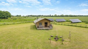 Un chalet rustique doté d’un porche, entouré d’un champ verdoyant et de panneaux solaires.