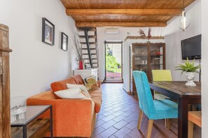 Un salon chaleureux avec un plafond en bois, un canapé, une table à manger avec des chaises, un téléviseur et un escalier.