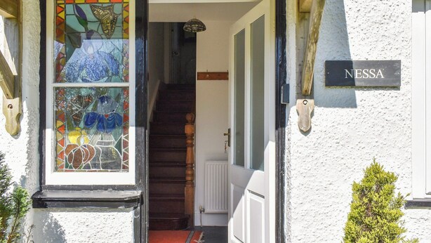 Une entrée d’immeuble avec une porte en vitrail, un escalier et une enseigne indiquant « NESSA ».