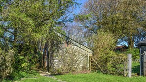 Un bâtiment en pierre, avec un chemin également en pierre menant à l’entrée, entouré de verdure et d’arbres.