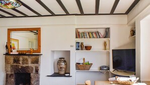 Un salon chaleureux avec une cheminée en pierre, une table en bois, un téléviseur et une bibliothèque remplie de livres et d’objets décoratifs.