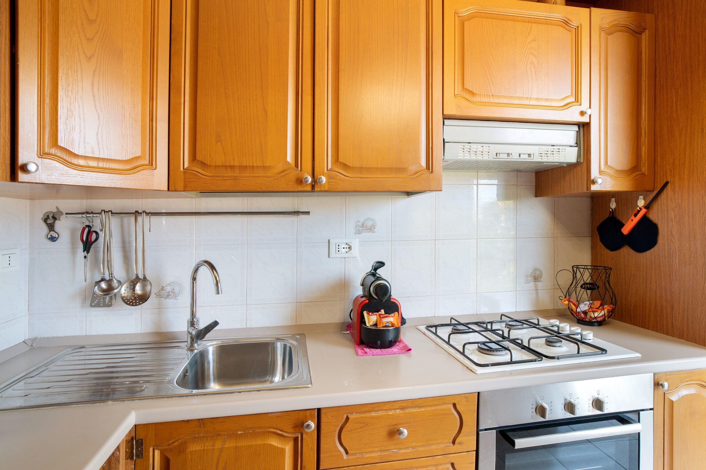 Una cocina con armarios de madera, un lavamanos de acero inoxidable, una estufa a gas y utensilios colgantes.
