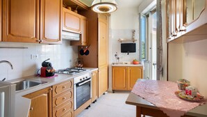 Een keuken met houten kastjes, een gasfornuis, een spoelbak en een tafel met een kantoneelkleed.