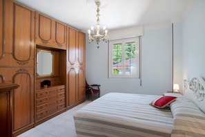 Une chambre à coucher avec un grand lit, une armoire en bois, un miroir, un lustre et une fenêtre donnant sur un beau paysage.