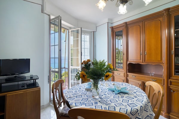 Un coin repas comprenant une table, des chaises, un téléviseur, des meubles en bois et une vue à travers une porte vitrée.