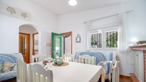 Un comedor con una mesa dispuesta para cuatro, sillas blancas, una puerta verde y una ventana con barrotes.