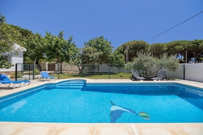 Una piscina con azulejos azules, rodeada de sillones de descanso y una valla.