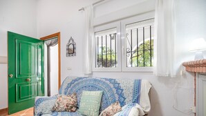 Una habitación con una puerta verde, un sofá estampado, una ventana con barrotes y una lámpara.
