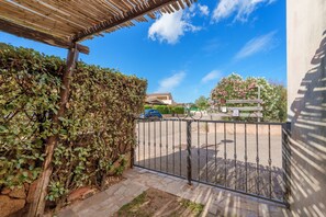 A gated entrance with a pergola, a hedge, and a view of a street with a car.