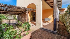 Un patio con una pérgola, una mesita y sillas, rodeado de plantas en macetas y un camino de ladrillos.