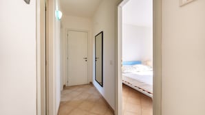 Un pasillo estrecho que conduce a un dormitorio con una cama, una puerta y un espejo instalado en la pared.