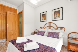 Un dormitorio con una cama de madera, ropa de cama blanca, dos cuadros en la pared y una mesita de noche de madera.