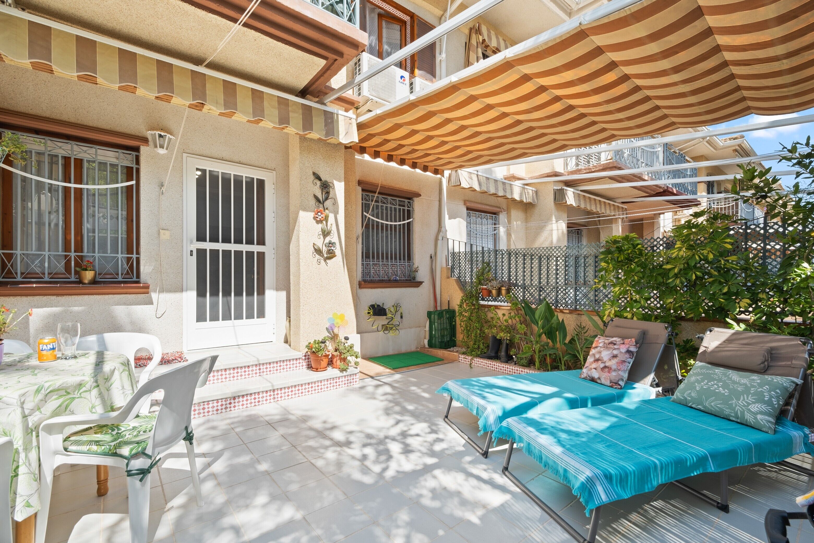 Une terrasse extérieure ensoleillée, avec une table, des chaises et un canapé recouvert d’un tissu à rayures.