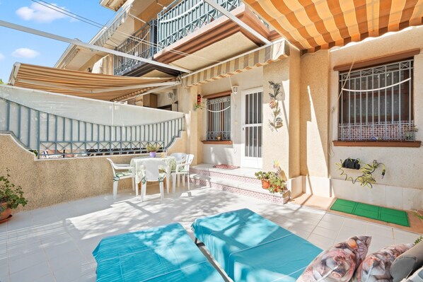 A covered outdoor area with a pool, lounge chairs, and a staircase leading to an upper level.