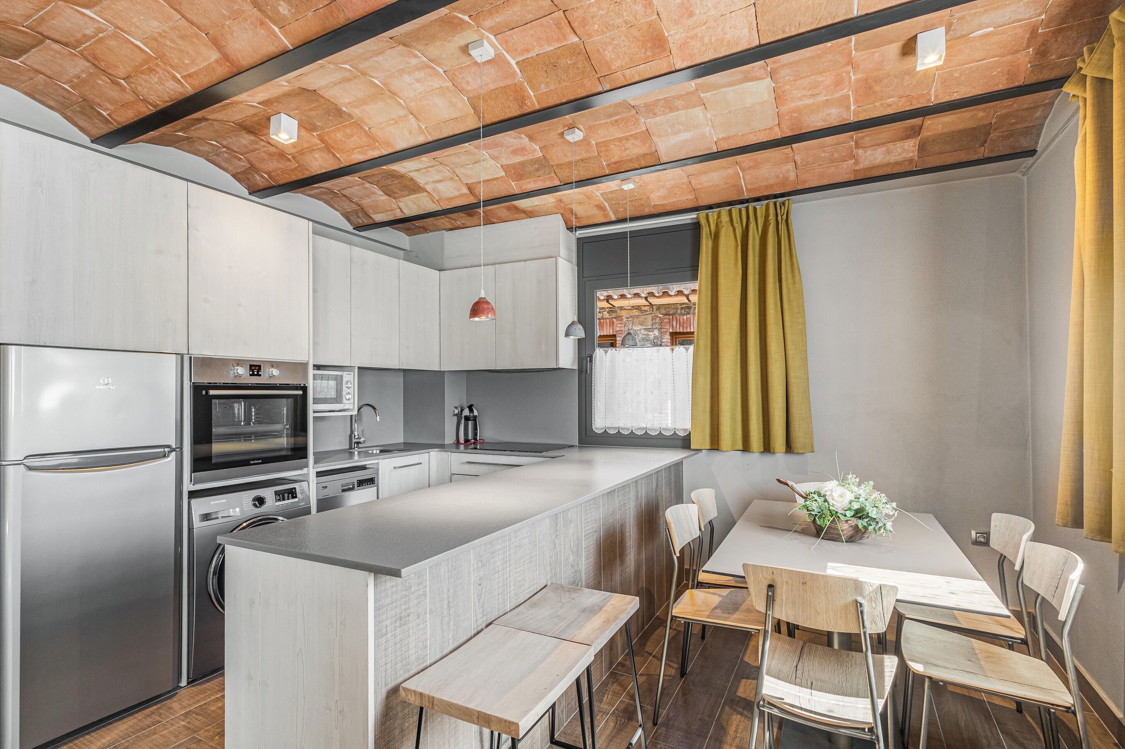 A modern kitchen with a central island, stainless steel appliances, and a dining area with wooden chairs and a table.
