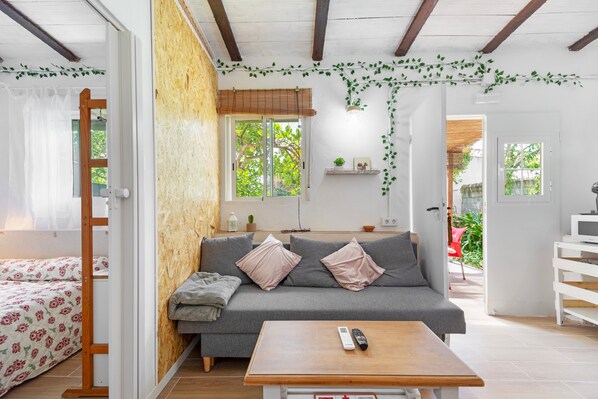 A cozy living room with a sofa, a wooden table, and a bed with floral bedding.