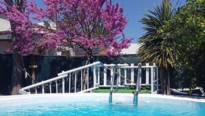 A swimming pool with a white deck, surrounded by trees and a fence.