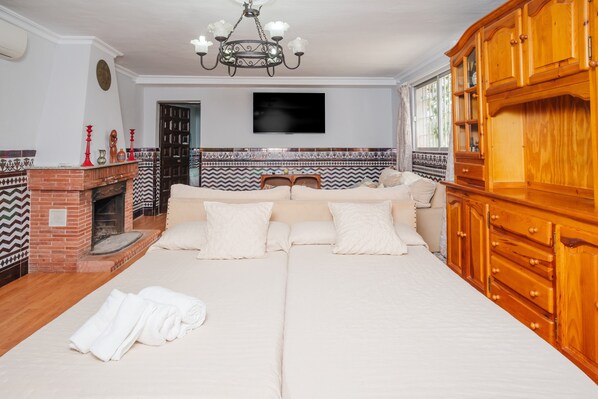 A bedroom with a large bed, a wooden wardrobe, a fireplace, and a television on the wall.