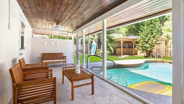Ein überdachter Patio-Bereich mit Pool, Holzmöbeln und Blick auf den Garten.