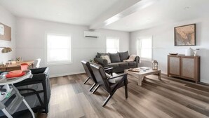 Ein geräumiges Wohnzimmer mit grauem Sofa, schwarzen Sesseln, einem Holztisch und einem Schrank.