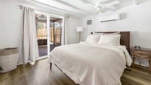 Ein Schlafzimmer mit einem großen Bett, einem Deckenventilator, einem Nachttisch und Blick ins Freie.