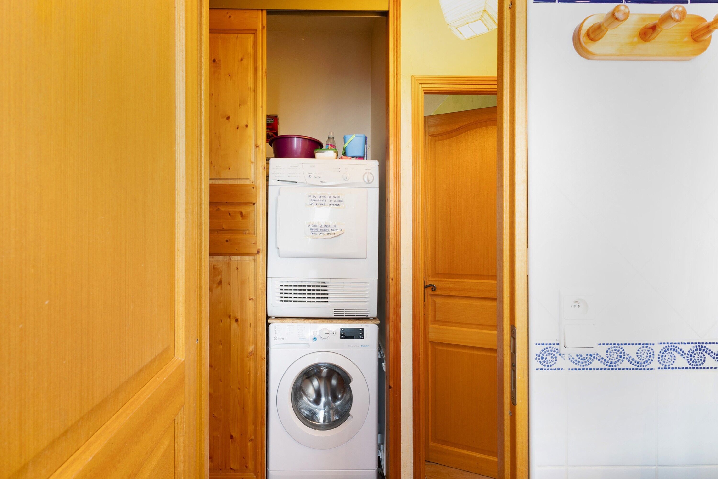 A laundry area with stacked appliances, a wooden door, and a tiled wall with a decorative border.