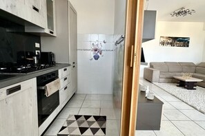 A modern kitchen with a stove, oven, and cabinets, leading to a living area with a sofa and a coffee table. - P034 - Porto Recanati, new three-room apartment with garden (Porto Recanati)