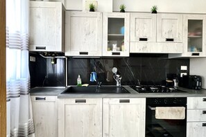 A kitchen with white wooden cabinets, a black countertop, a stove, and a sink.