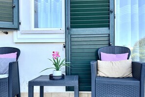 A patio with two wicker chairs, a small table with a potted plant, and a green door. - P034 - Porto Recanati, new three-room apartment with garden (Porto Recanati)