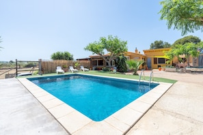 Une piscine rectangulaire dont le bord est recouvert de carreaux, entourée d’une terrasse en béton.