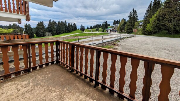 Ein Balkon mit Blick auf einen Kiesbereich, Bäume und ein entferntes Gebäude.