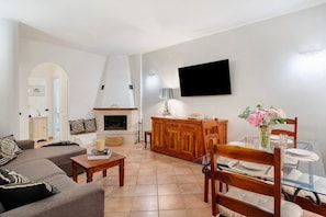 Een woonkamer met een bank, salontafel, televisie, open haard, eettafel en stoelen.