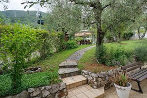 Un jardín con un sendero de piedra, un banco de madera y un pabellón.