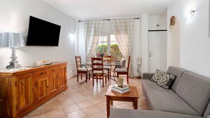 Een woonkamer met een bank, een salontafel, een televisie, een eettafel met stoelen en een kast.