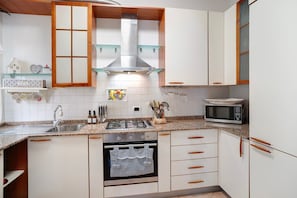 Una cocina con gabinetes blancos, estufa a gas, microondas y campana extractora de acero inoxidable.