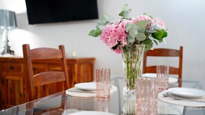 Een eettafel met een transparante glazen blad, roze drinkglazen en een vaas met roze bloemen.