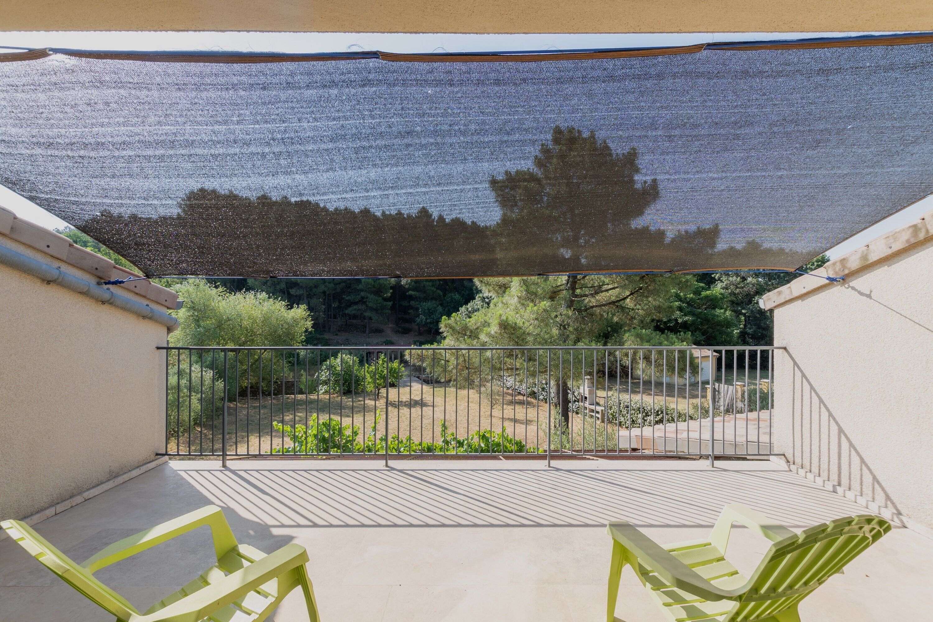 A balcony with a mesh shade, metal railing, and two green chairs.