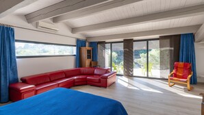 A modern room with a large bed, a red sofa, a wooden cabinet, and a balcony with chairs. - Villa "Luminières I" with Mountain View, Private Pool & Wi-Fi (Les Salelles)