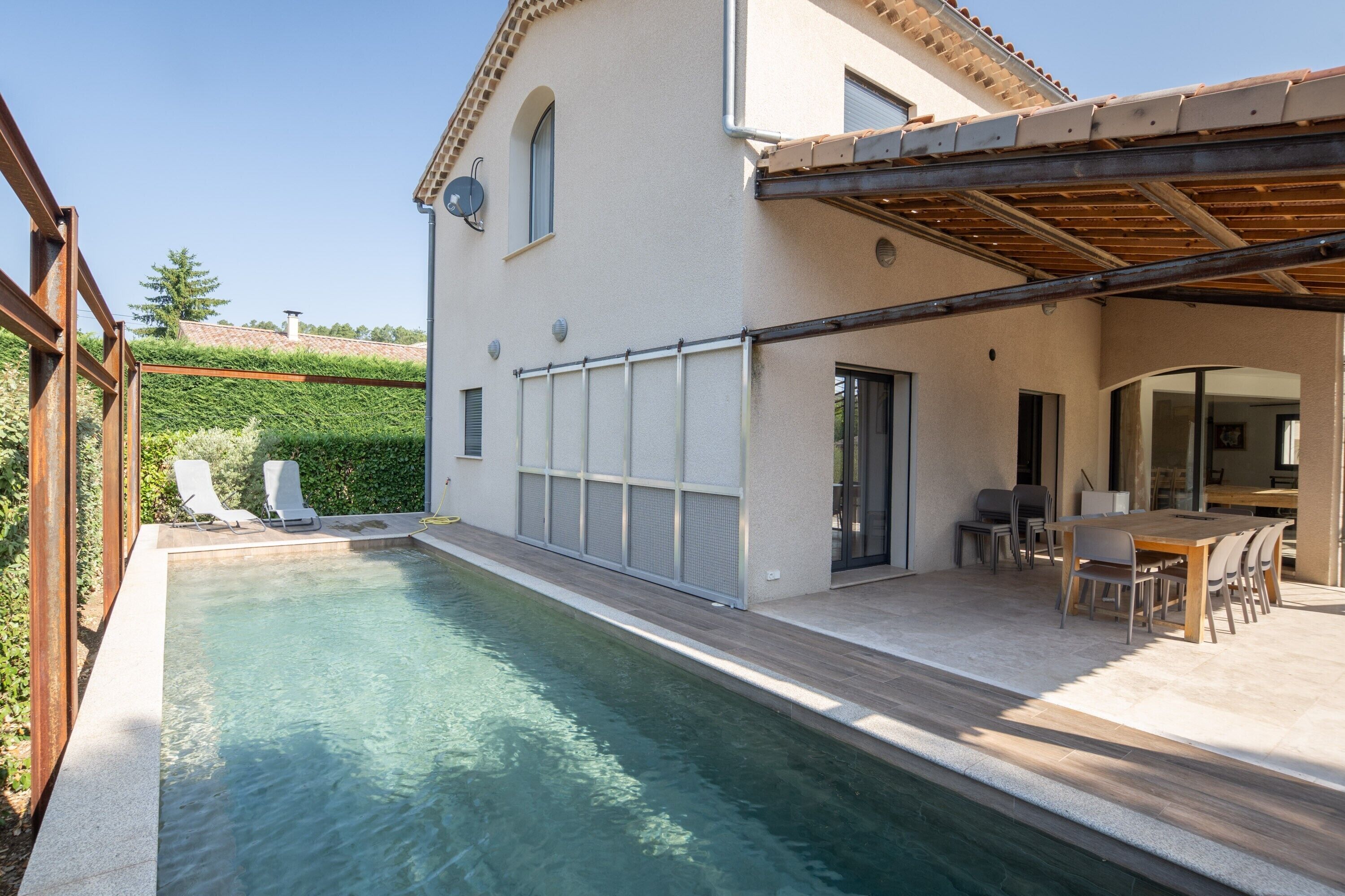 A modern house with a swimming pool, a covered patio, and a dining area.