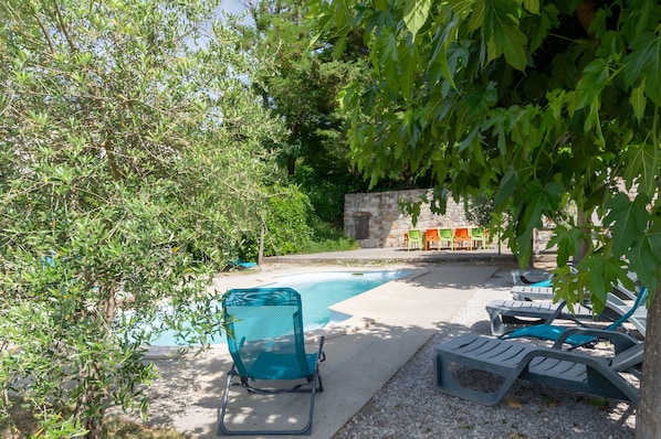 A pool area with lounge chairs, a stone wall, and greenery.