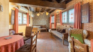 A rustic interior with stone walls, wooden beams, a round table, and comfortable seating. - Holiday Home 'Casa Alval' with Mountain View, Wi-Fi and Air Conditioning (VILLACASTIN)