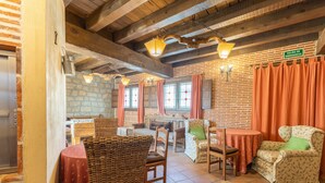 A rustic interior with exposed wooden beams, a brick wall, and a dining area with wicker furniture and a table. - Holiday Home 'Casa Alval' with Mountain View, Wi-Fi and Air Conditioning (VILLACASTIN)