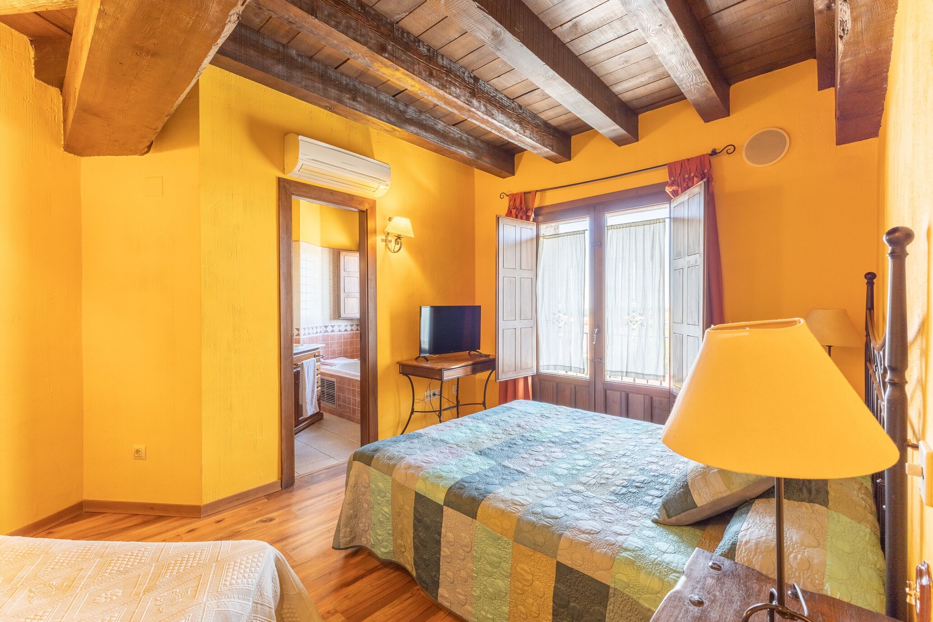 Un dormitorio con cama, escritorio, lámpara y ventana con cortinas.