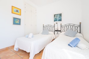 A room with two beds, white bedding, a metal headboard, and two framed pictures on the wall.