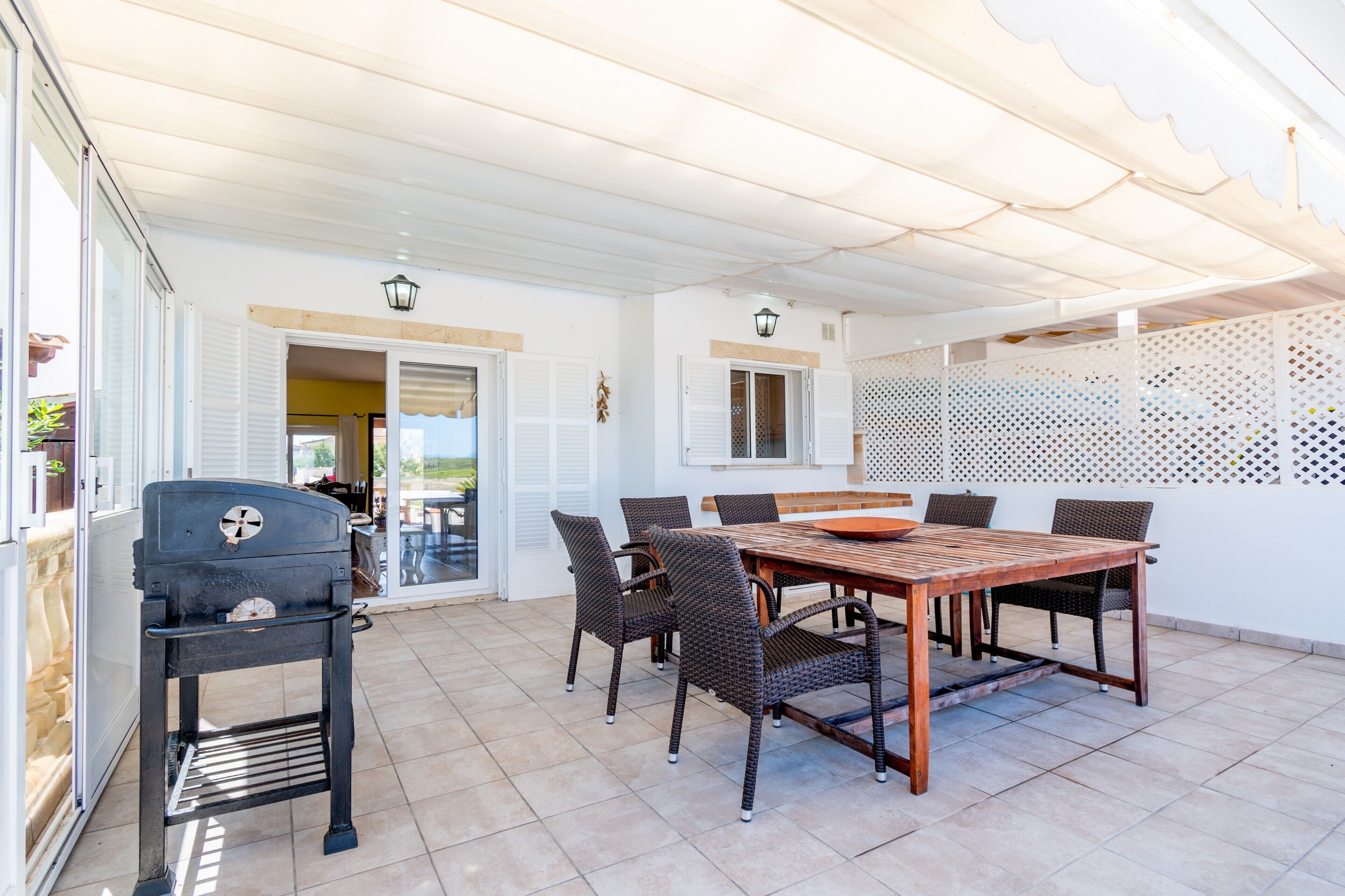Una terrazza esterna con tavolo in legno e sedie in vimini, un barbecue e un tetto coperto.